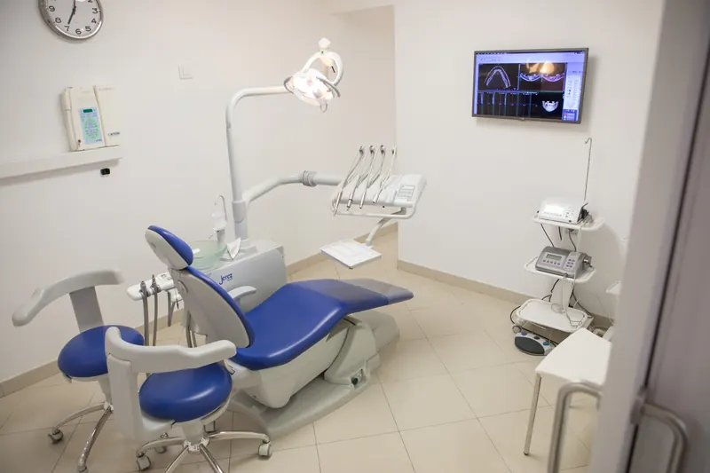 Gabinete dental con sillón azul y pantalla en la pared