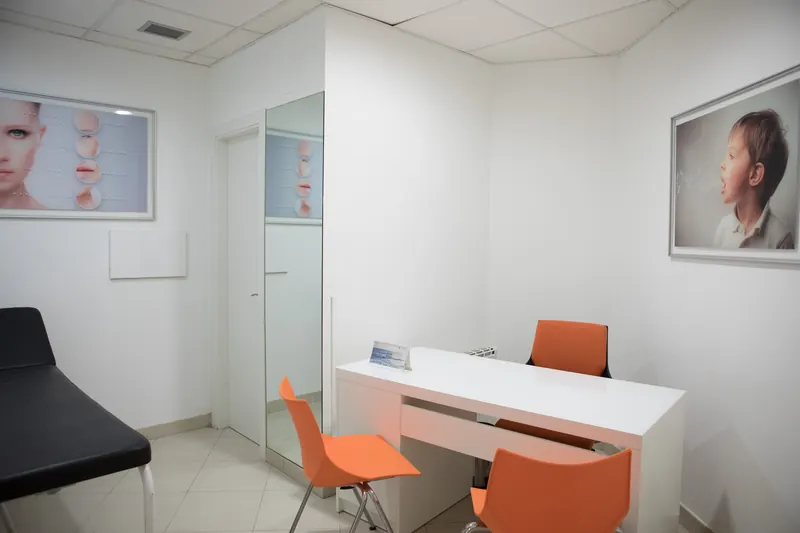 Gabinete de logopedia con mesa blanca, sillas naranjas y camilla