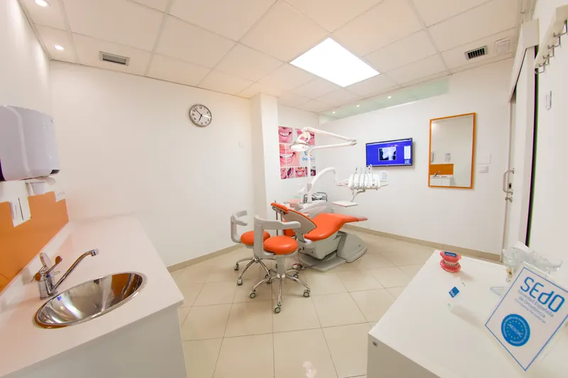 Gabinete dental con sillón naranja, lavabo y pantalla de radiografías