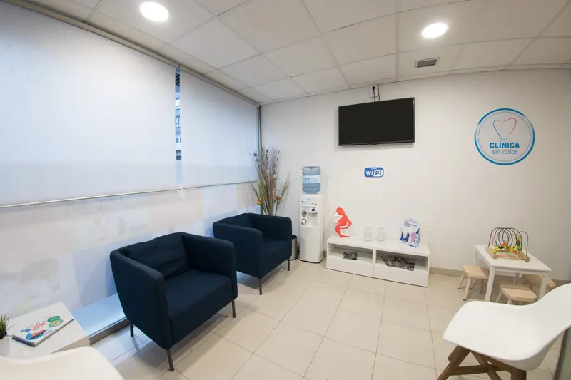 Sala de espera con butacas azules, televisión y rincón infantil